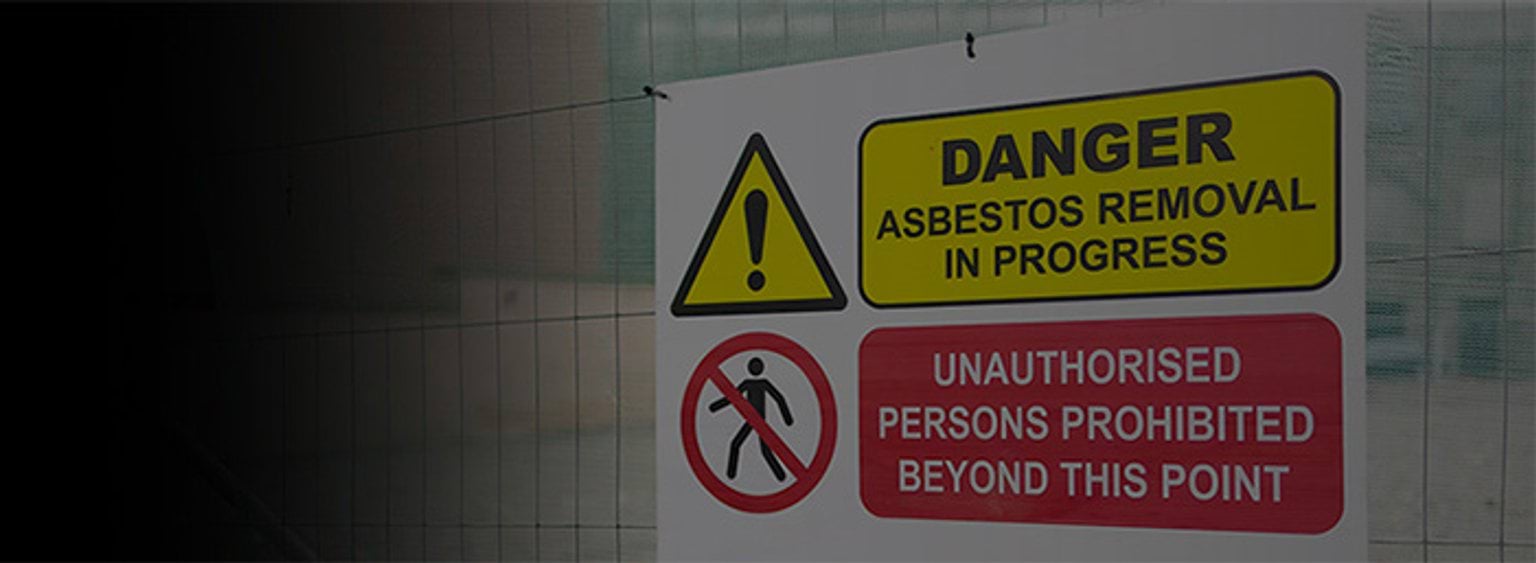 2 signs on a site perimeter fence. Sign 1 reads: Danger - Asbestos removal in progress. Sign 2 reads: Unauthorised persons prohibited beyond this point.